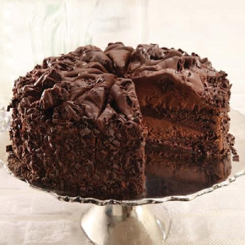 A rich chocolate cake with layers and chocolate shavings, partially sliced on a silver cake stand.