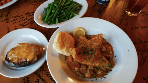 A plate with fried fish, a biscuit, gumbo, and a side of green beans, with a baked potato topped with cheese.