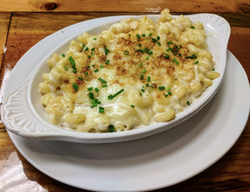 Creamy macaroni and cheese baked with a golden crust, garnished with chopped chives, served in a white dish.