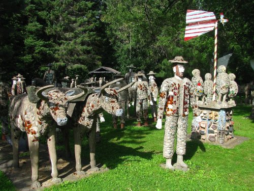 A whimsical outdoor sculpture garden featuring stone animals and human figures, surrounded by trees and greenery.