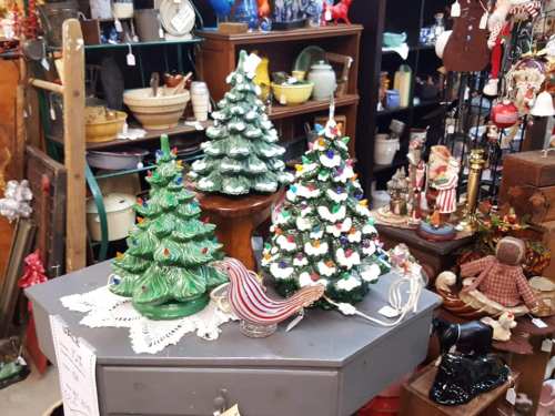A display of vintage ceramic Christmas trees and decorative items on a table in an antique shop.