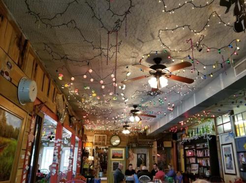 Cozy restaurant interior with colorful string lights, fans, and rustic decor, featuring patrons enjoying their meals.