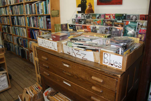A wooden drawer unit with labeled boxes for classical, jazz, and blues CDs, surrounded by shelves of books.