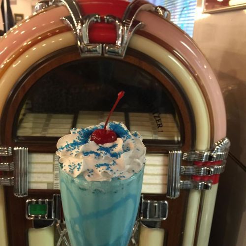 A colorful milkshake topped with whipped cream and a cherry, in front of a vintage jukebox.