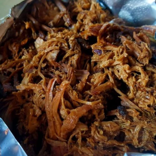 Close-up of tender, shredded meat in a foil container, showcasing a rich, brown color and juicy texture.