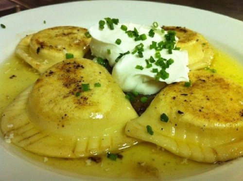 Plate of golden-brown pierogi topped with sour cream and chives, drizzled with melted butter.