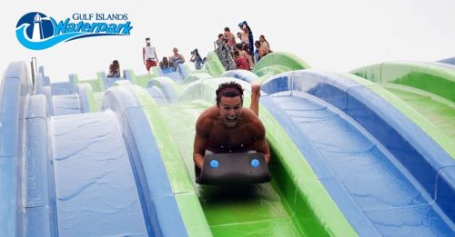 A person slides down a colorful water slide at Gulf Islands Waterpark, surrounded by splashing water and other visitors.