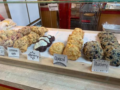 A display of various scones, including blueberry, apricot, elderberry, cinnamon apple, and more, on a countertop.