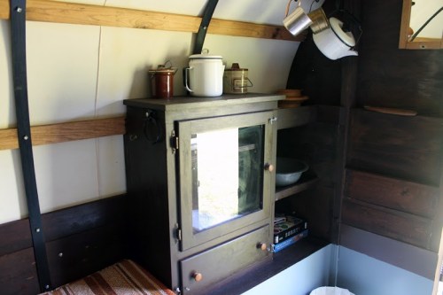 Cozy interior of a small cabin featuring a wooden cabinet, shelves, and kitchenware.