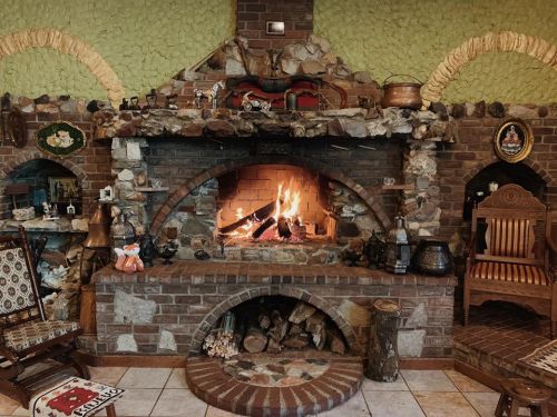 Cozy stone fireplace with a roaring fire, surrounded by rustic decor and wooden furniture in a warm, inviting room.