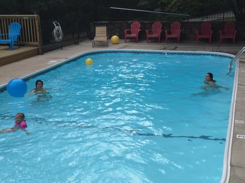Two adults and a child swim in a blue pool, with colorful beach balls and lounge chairs nearby.