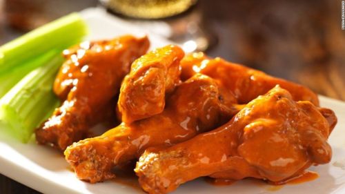 A plate of spicy chicken wings glazed in sauce, accompanied by celery sticks.