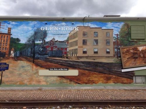 Mural depicting Glen Rock, Pennsylvania, featuring a train, buildings, and historical elements on a green wall.