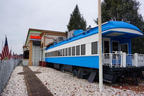 A blue train car diner next to a restaurant, surrounded by white gravel and American flags.