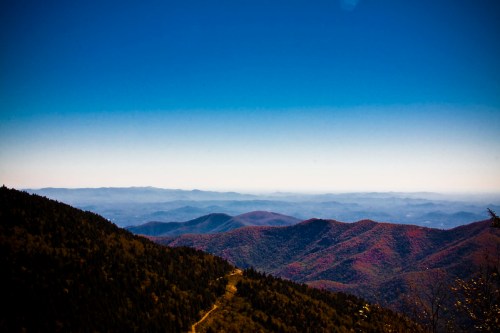 A panoramic view of rolling mountains with autumn foliage under a clear blue sky.