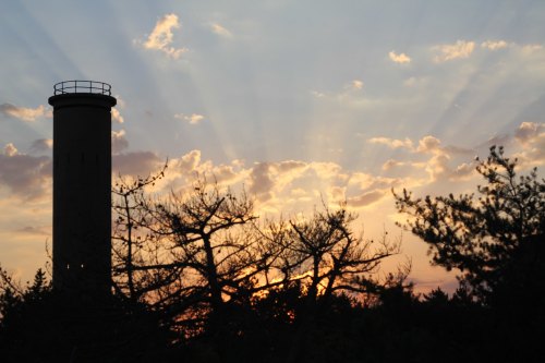 Silhouette of a tower and trees against a sunset with rays of light breaking through the clouds.