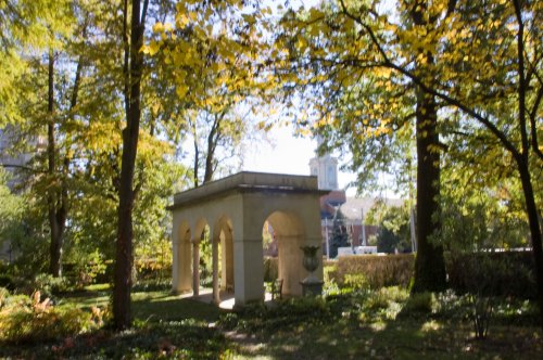 A serene garden scene featuring a stone structure with arches, surrounded by trees and colorful autumn leaves.
