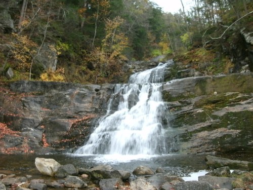 A serene waterfall cascading over rocky terrain, surrounded by autumn foliage and trees.