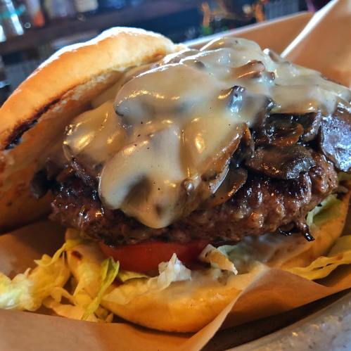 Close-up of a juicy burger with melted cheese, sautéed mushrooms, lettuce, and tomato on a toasted bun.
