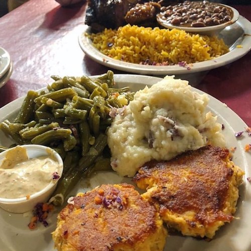 A plate of food featuring green beans, mashed potatoes, cornbread, and a side of dipping sauce.