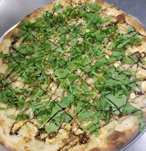 A freshly baked pizza topped with arugula, cheese, and a drizzle of balsamic glaze on a golden crust.