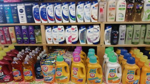 Shelves stocked with various brands of shampoos, conditioners, and laundry detergents in colorful bottles.