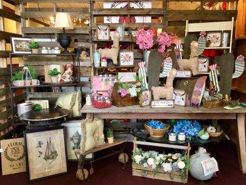 A rustic display of home decor items, including flowers, pillows, and vintage-style accessories on wooden shelves.