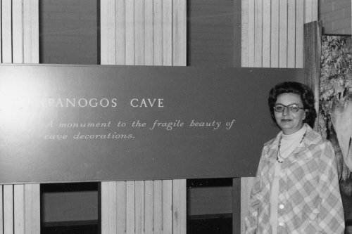 A woman stands beside a sign for "Timpanogos Cave," highlighting the beauty of cave decorations.