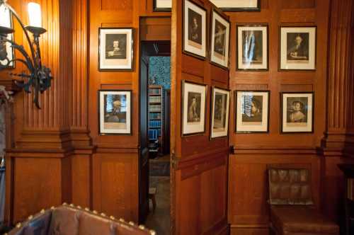 A wooden door opens to a room lined with framed portraits on the walls, showcasing a cozy library atmosphere.