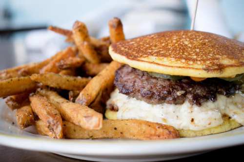 A close-up of a burger with a beef patty, pickles, and creamy sauce, served with a side of golden fries.