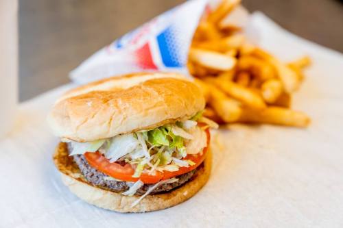 A hamburger with lettuce and tomato beside a serving of crinkle-cut fries on a white paper surface.
