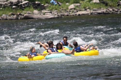 A group of six people enjoying a fun day of tubing on a river, surrounded by greenery and splashing water.