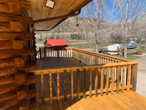A wooden deck with a railing overlooks a grassy area and parked RVs, surrounded by trees and mountains in the background.