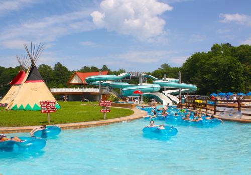 A water park scene with a slide, lazy river, and a teepee, featuring people floating on tubes under a blue sky.