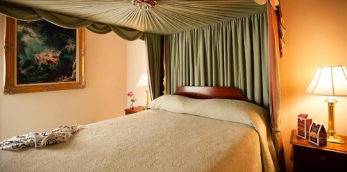 Cozy bedroom with a canopy bed, elegant drapes, a painting, and bedside lamps.