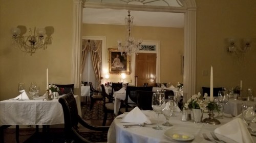 Elegant restaurant interior with white tablecloths, candlelight, and chandeliers, creating a warm, inviting atmosphere.