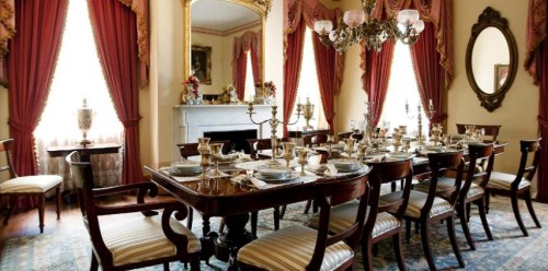 Elegant dining room with a large wooden table set for a meal, surrounded by ornate curtains and classic decor.