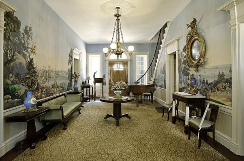 Elegant foyer with vintage decor, muraled walls, a chandelier, and a grand piano, featuring a floral centerpiece.