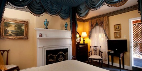 Cozy bedroom with a four-poster bed, elegant drapes, a fireplace, and vintage decor.