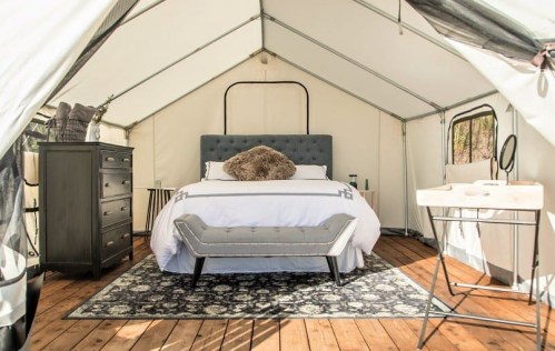Cozy glamping tent interior featuring a bed, dresser, and stylish decor on wooden flooring.