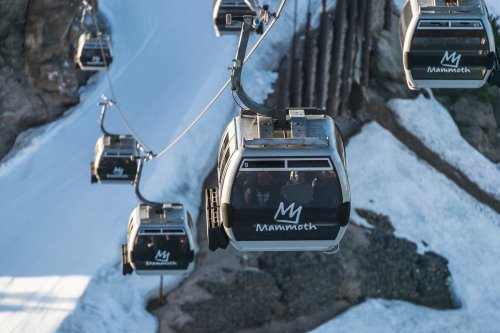 A row of gondolas on a ski lift above snowy terrain, with the word "Mammoth" visible on the cabins.