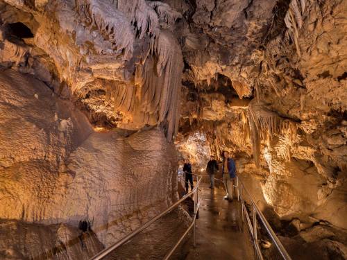 Visitors explore a cave with stunning stalactites and stalagmites, illuminated by warm lighting along a walkway.