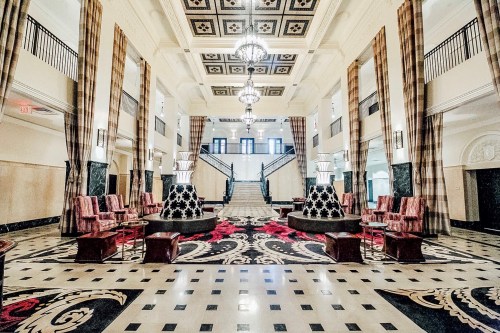 Elegant hotel lobby featuring ornate chandeliers, patterned carpet, and stylish seating around decorative columns.