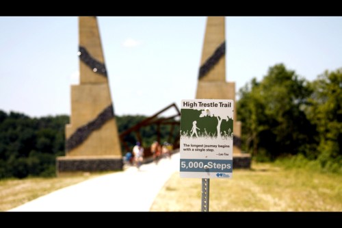 Sign for High Trestle Trail with a quote about journeys, set against a background of a trail and people walking.