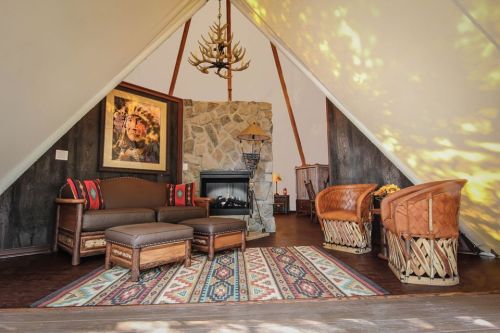 Cozy interior of a tent-style room with a stone fireplace, seating area, and decorative rug. Warm, inviting atmosphere.