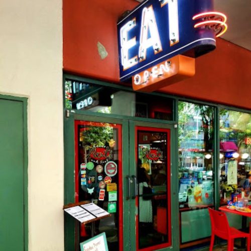A colorful restaurant entrance with a neon "EAT" sign and open door, featuring stickers and a menu outside.