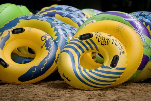 A colorful pile of inflatable river tubes in yellow, green, and blue, resting on a sandy surface.