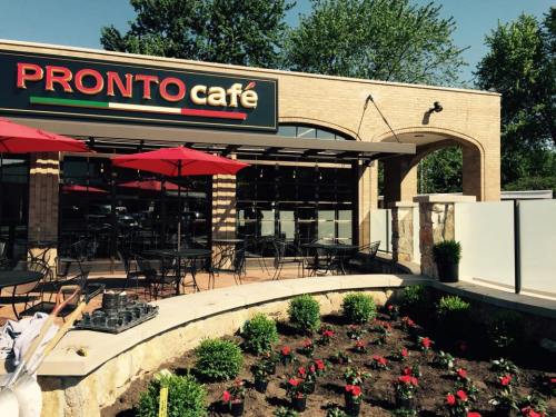 Exterior of Pronto Café with outdoor seating, red umbrellas, and a landscaped garden in front.