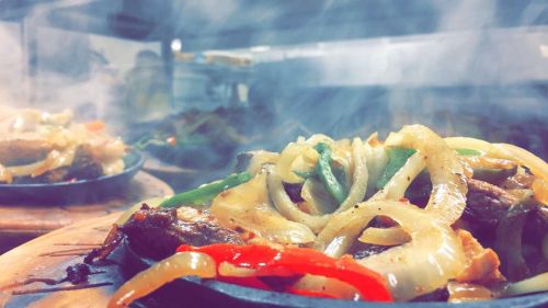 Sizzling fajitas with grilled meat, onions, and bell peppers, emitting steam on a hot skillet.