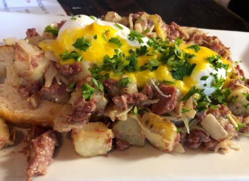 A plate of corned beef hash topped with two poached eggs and fresh herbs, served on toasted bread.